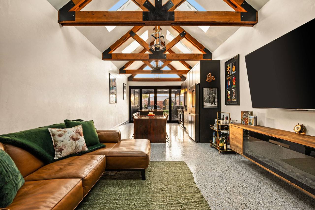 Open-plan living and kitchen area in a completed home — level polished-concrete floor, a wide clear walkway and a raked timber-truss ceiling.